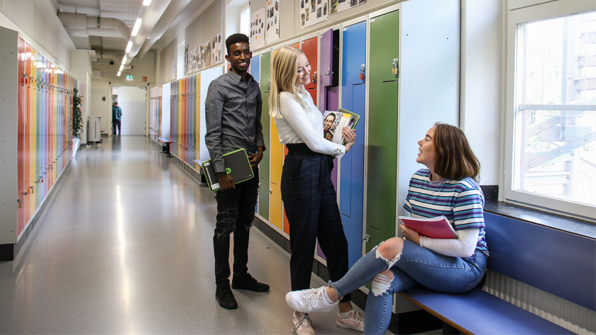 Tre elever i en skolkorridor med färgglada skåp
