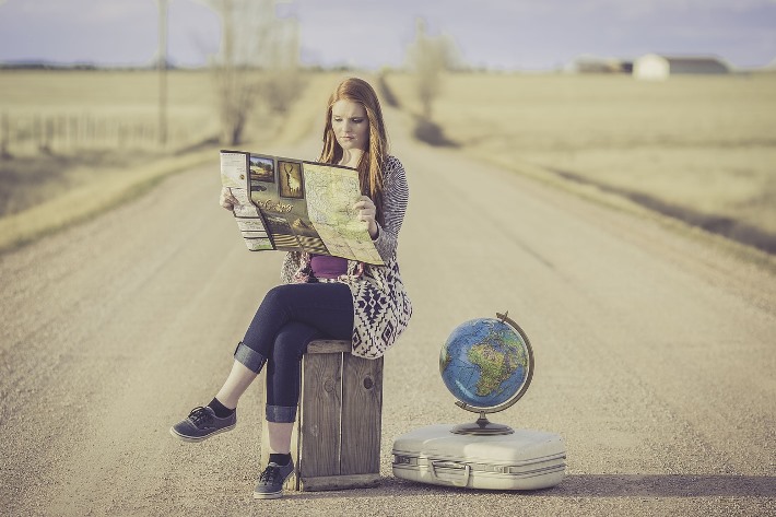 En ungdom med karta och resväska, som sitter på en öde väg.