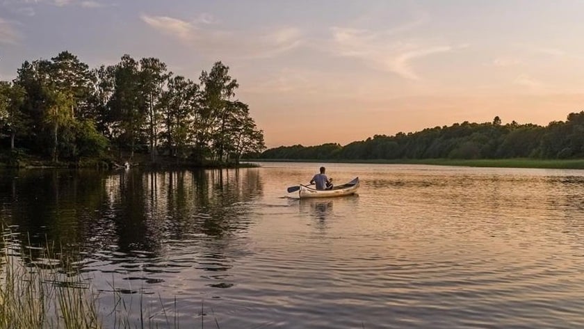 Person som paddlar i kanot på vatten i solnedgång