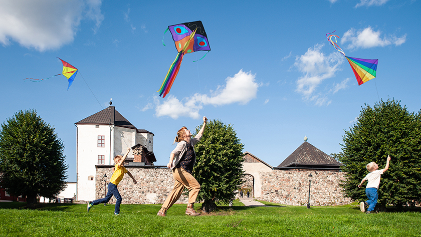Tre personer som springer med var sin flygande drake, framför Nyköpings slott