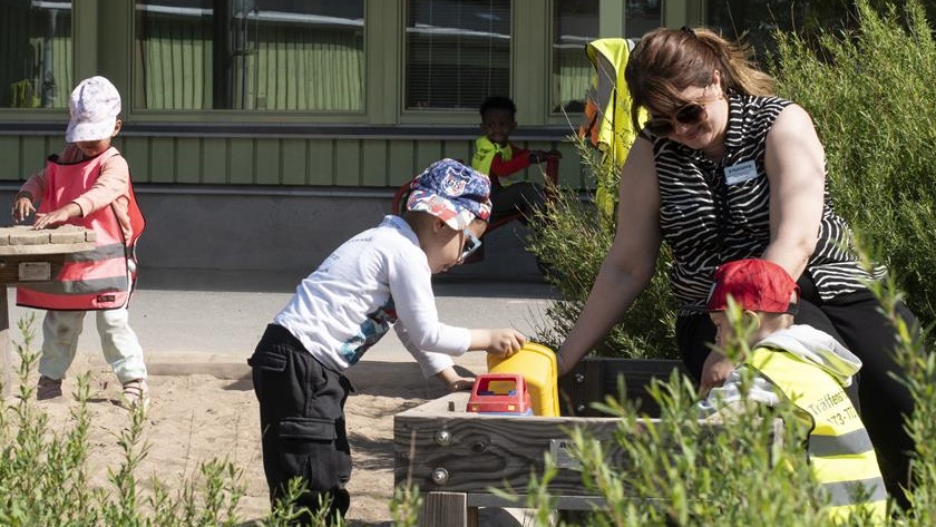 Två barn och en pedagog som gräver i ett land på en förskolegård