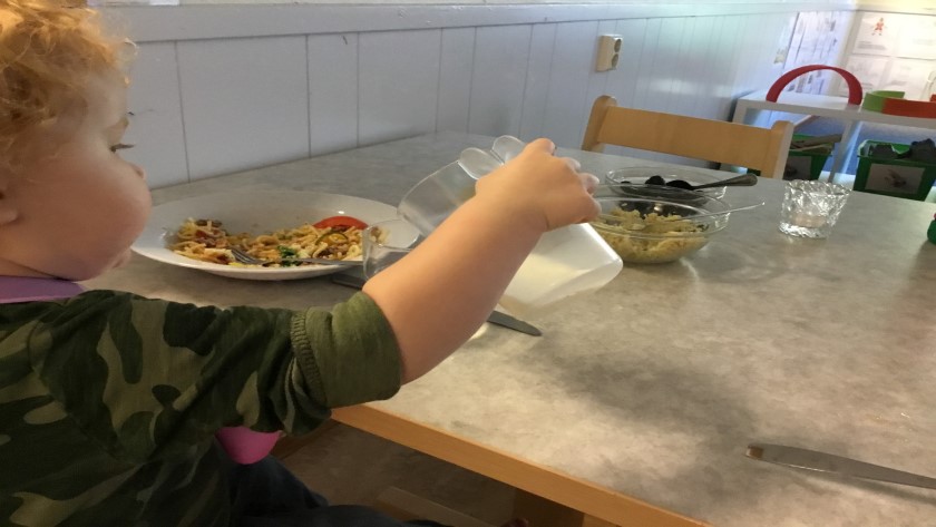 Barn äter mat och häller upp mjölk i glas själv