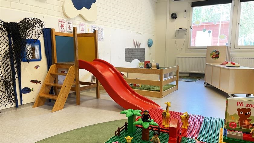 Del av ett rum inne på förskola med liten rutschkana och lego. 