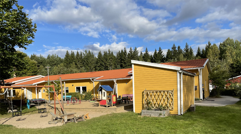 Den gula förskolebyggnaden och dess utegård med gungor