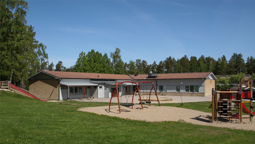 Bild på skolbyggnaden för Dammlötskolan i gult tegel som en L form, lekplats framför