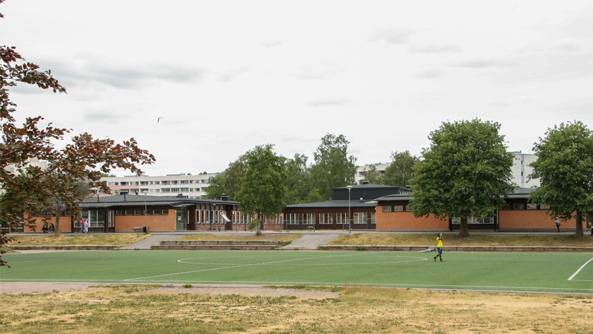 Byggnaden för Gruvans skola Brandkärr, brunröd låg tegelbyggnad, fotbollsplan i förgrunden