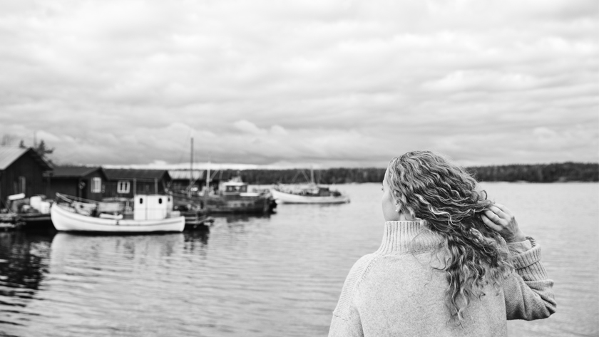 svartvit bild på tjej bakifrån som tittar ut över vatten och båtar