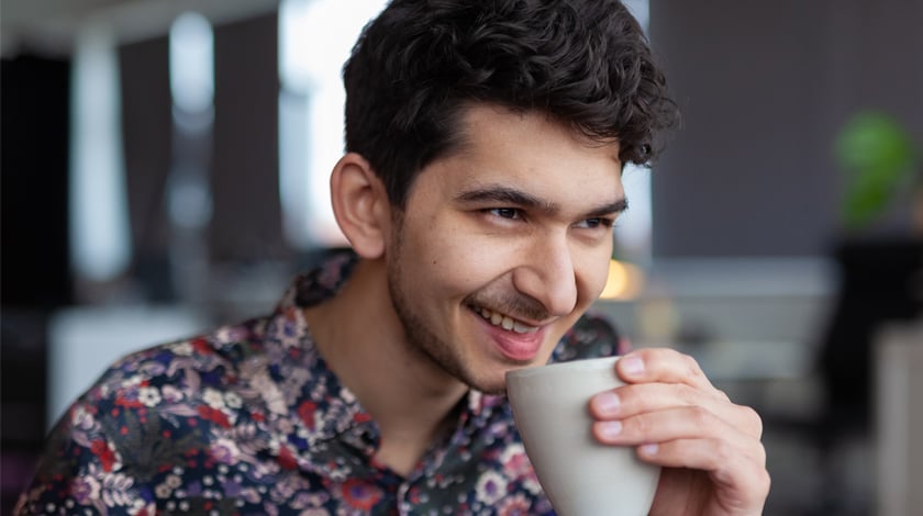 Porträtt på John Venkiah som håller i en kaffekopp framför munnen