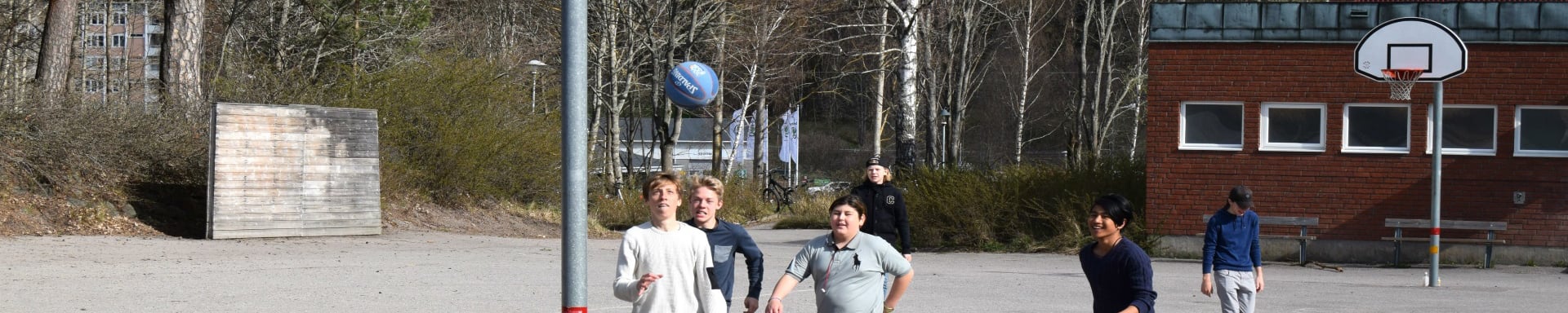 Elever spelar basket på skolgård framför skolbyggnad