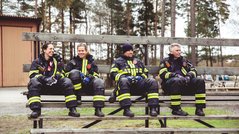 Två brandmän, en kvinna och en man, som är klädda i hälften larmställ och hälften vanliga kläder